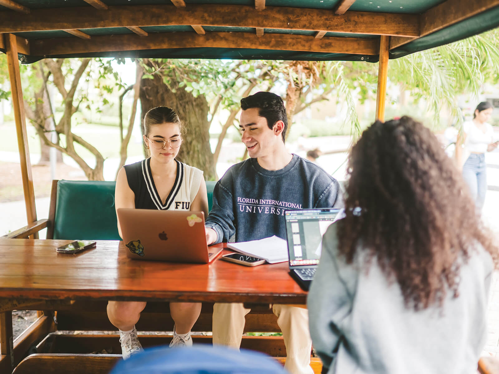 A photo of three students sitting in a cabana with their laptops. 
