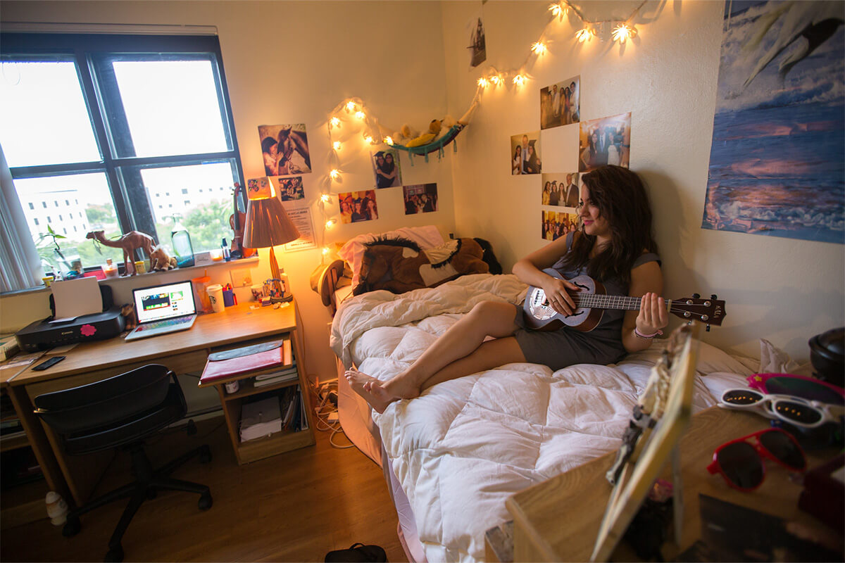 An FIU student sitting in her dorm playing the guitar