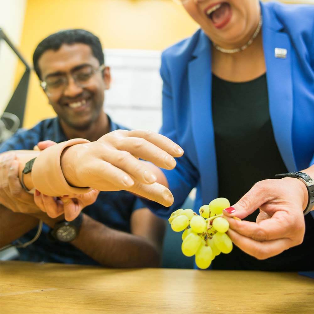 An FIU student with Dr. Jung showing the neural-enabled prosthetic hand grabbing grapes. 